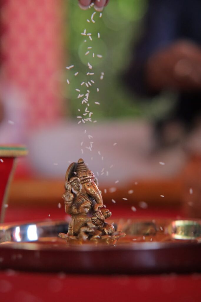 pexels photo 36854242 A small Ganesh statue on a tray with rice raining down during a traditional ceremony.
